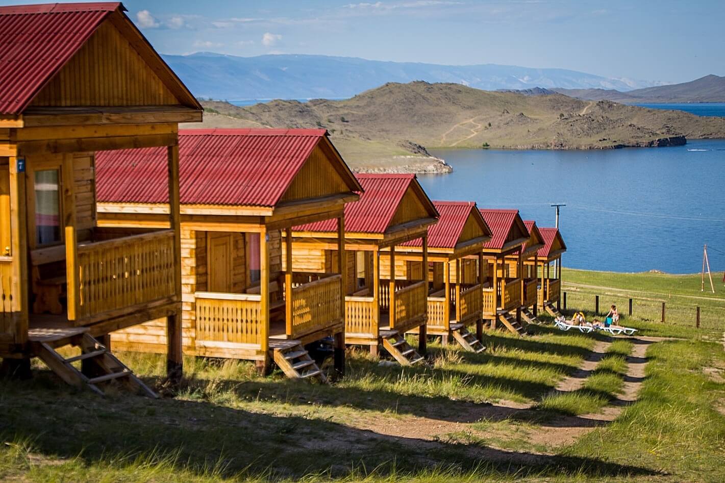 Расположенные в ряд, небольшие, деревянные домики. Вдалеке - Байкал.