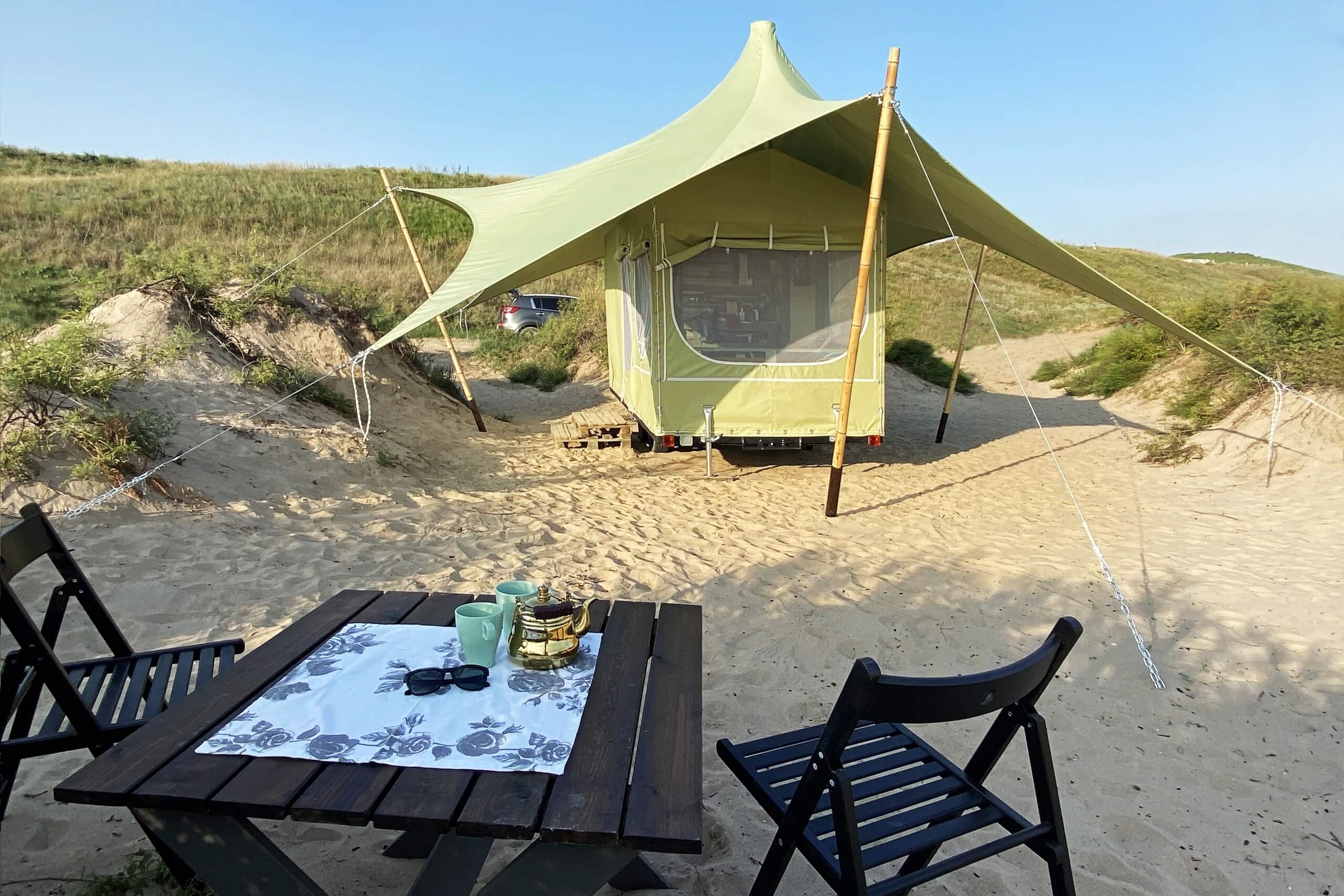 Пляж, домик-палатка и столик со стульями.