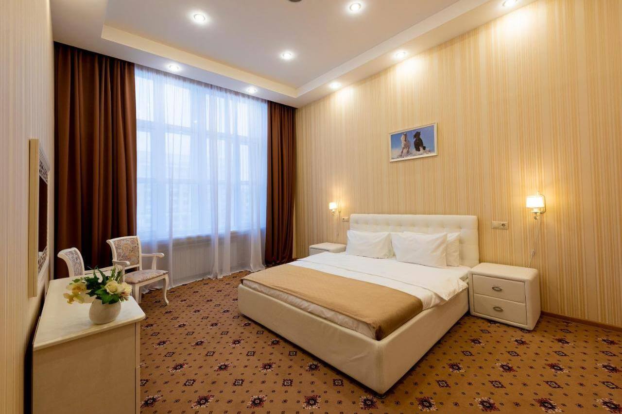 Интерьер гостиничного номера: большая, двуспальная кровать с прикроватными тумбочками, зеркало и комод.