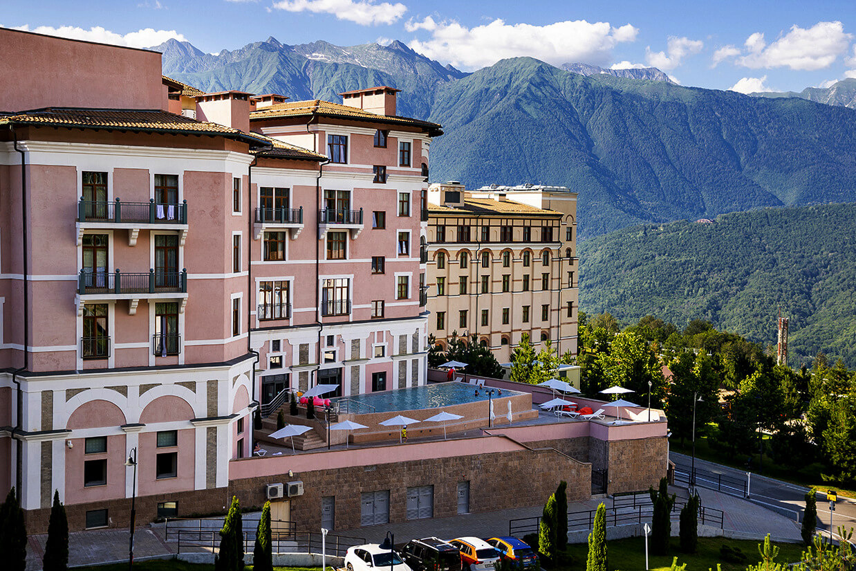 Здание отеля, бассейн и Кавказские горы.
