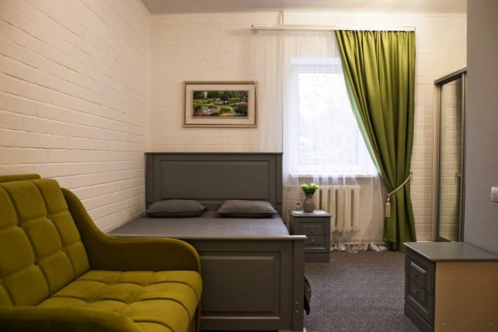 В номере: серая кровать, оливковые шторы и диван.