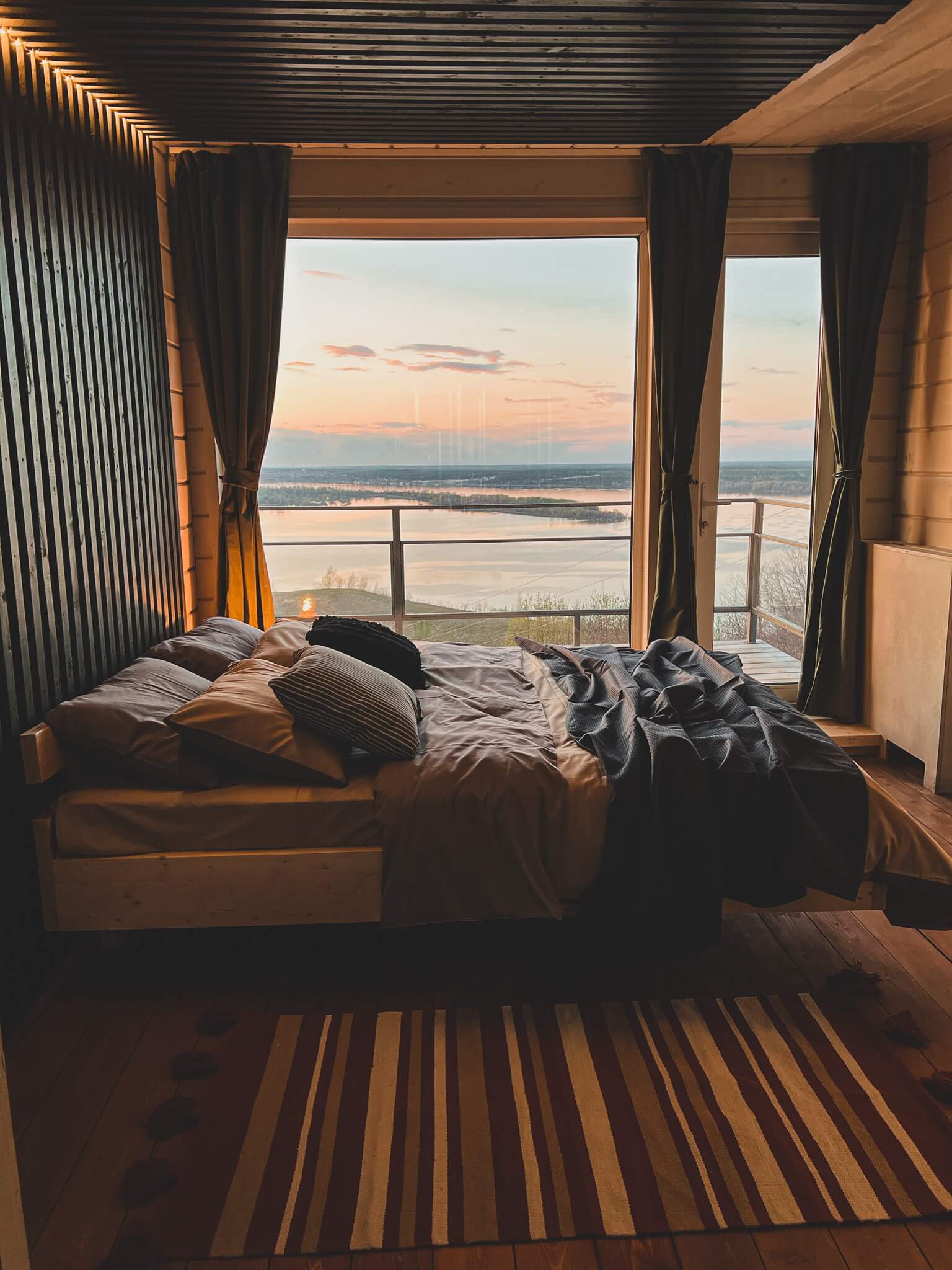 Большая, двуспальная кровать расположена возле панорамного окна.