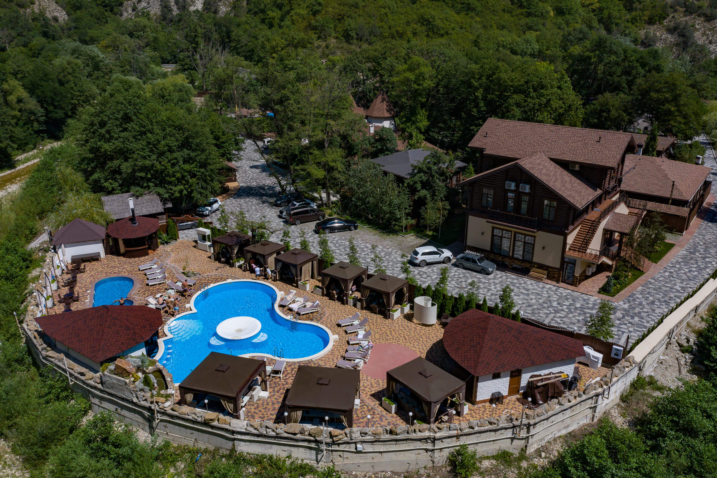 Панорамный вид на территорию комплекса: бассейн, беседки для отдыха, гостевой дом с парковкой.