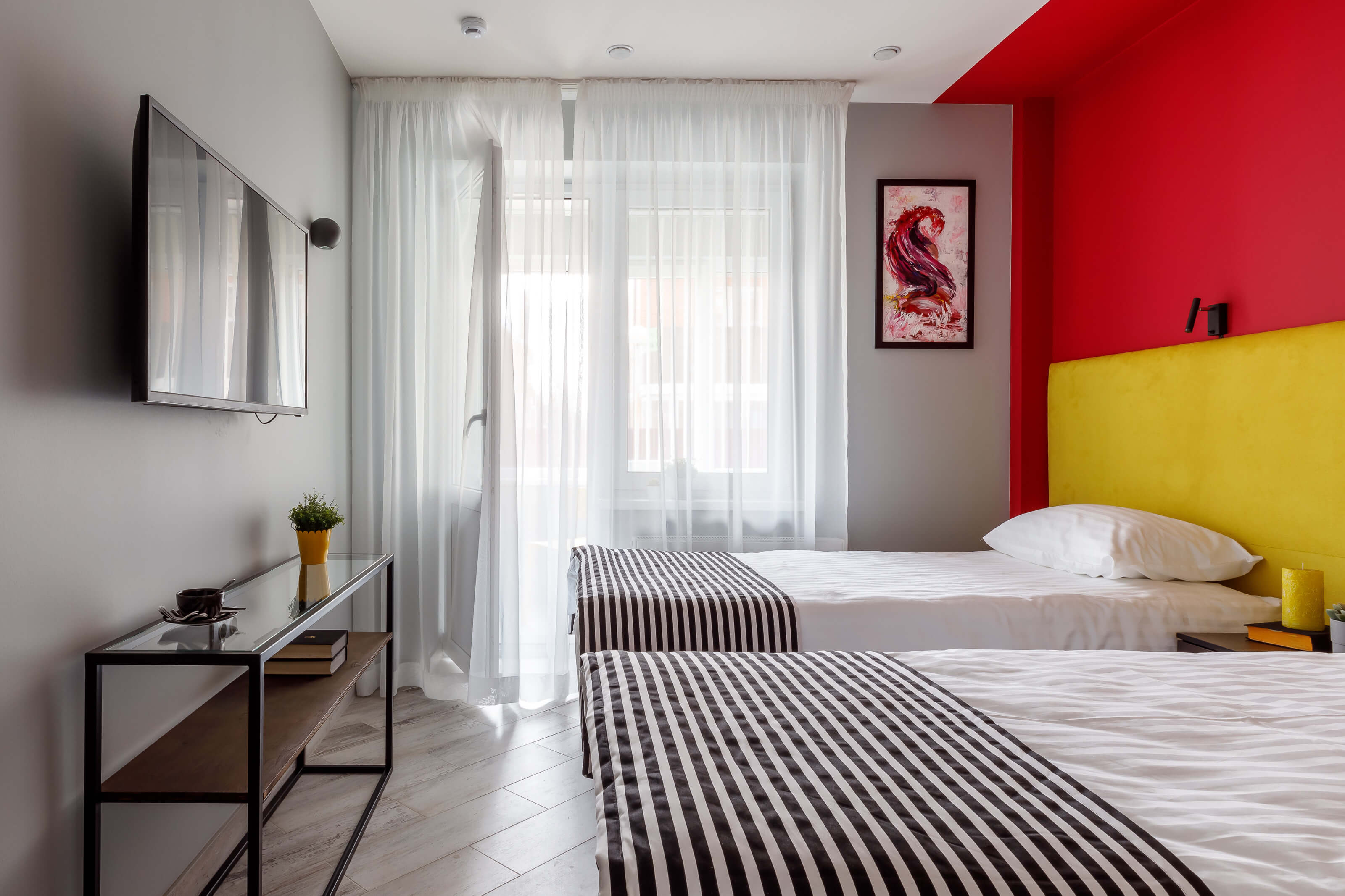 Стена выкрашена в яркие красный и желтый цвет. На кровати полосатые черно-белые саше.