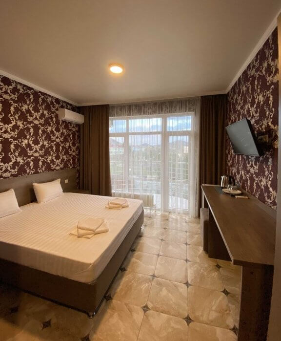 Пример интерьера гостиничного номера: большая кровать, телевизор и стол для работы. Преобладают коричневые и темно-бордовые оттенки.