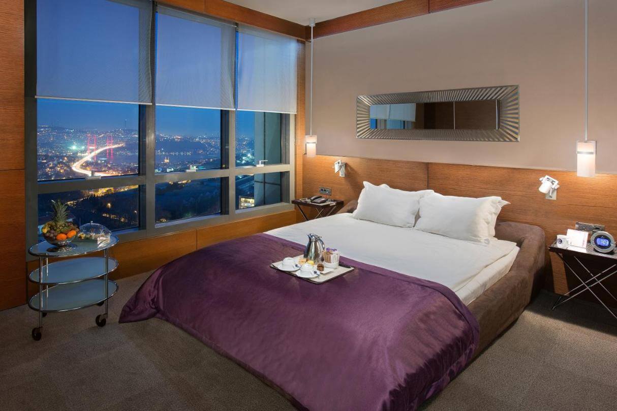 Возле окна стоит большая двуспальная кровать, накрытая фиолетовым саше.