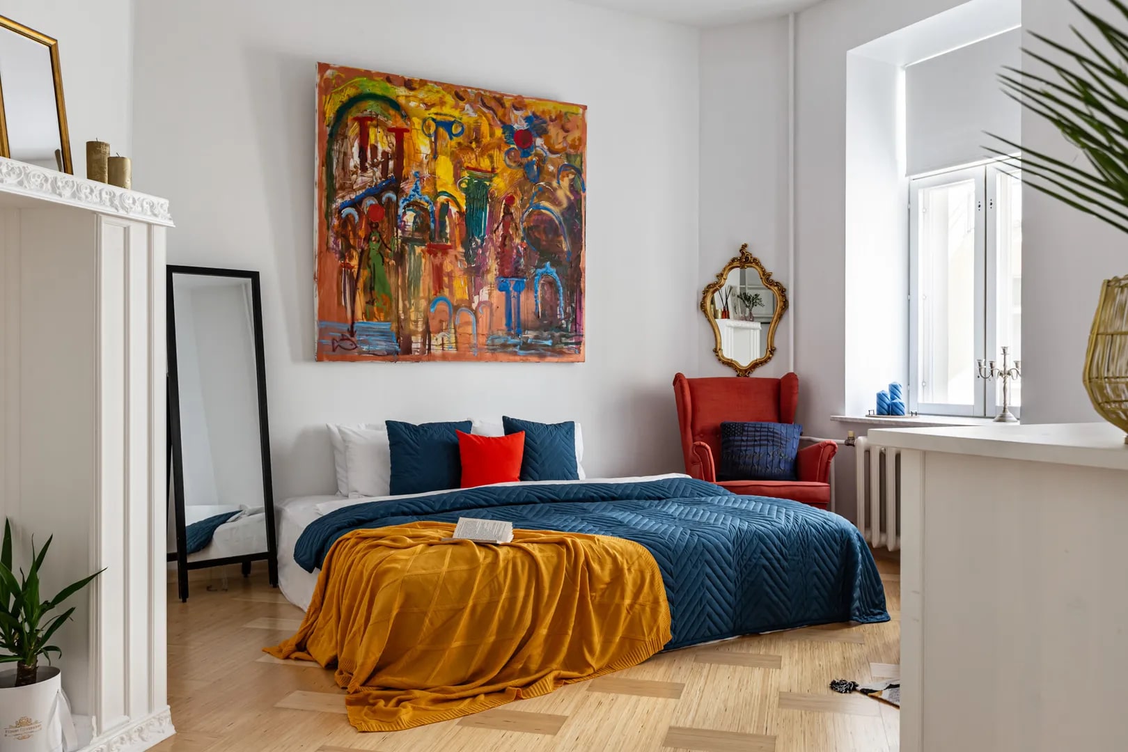 Кровать застелена цветным покрывалом, на стене - современное искусство.