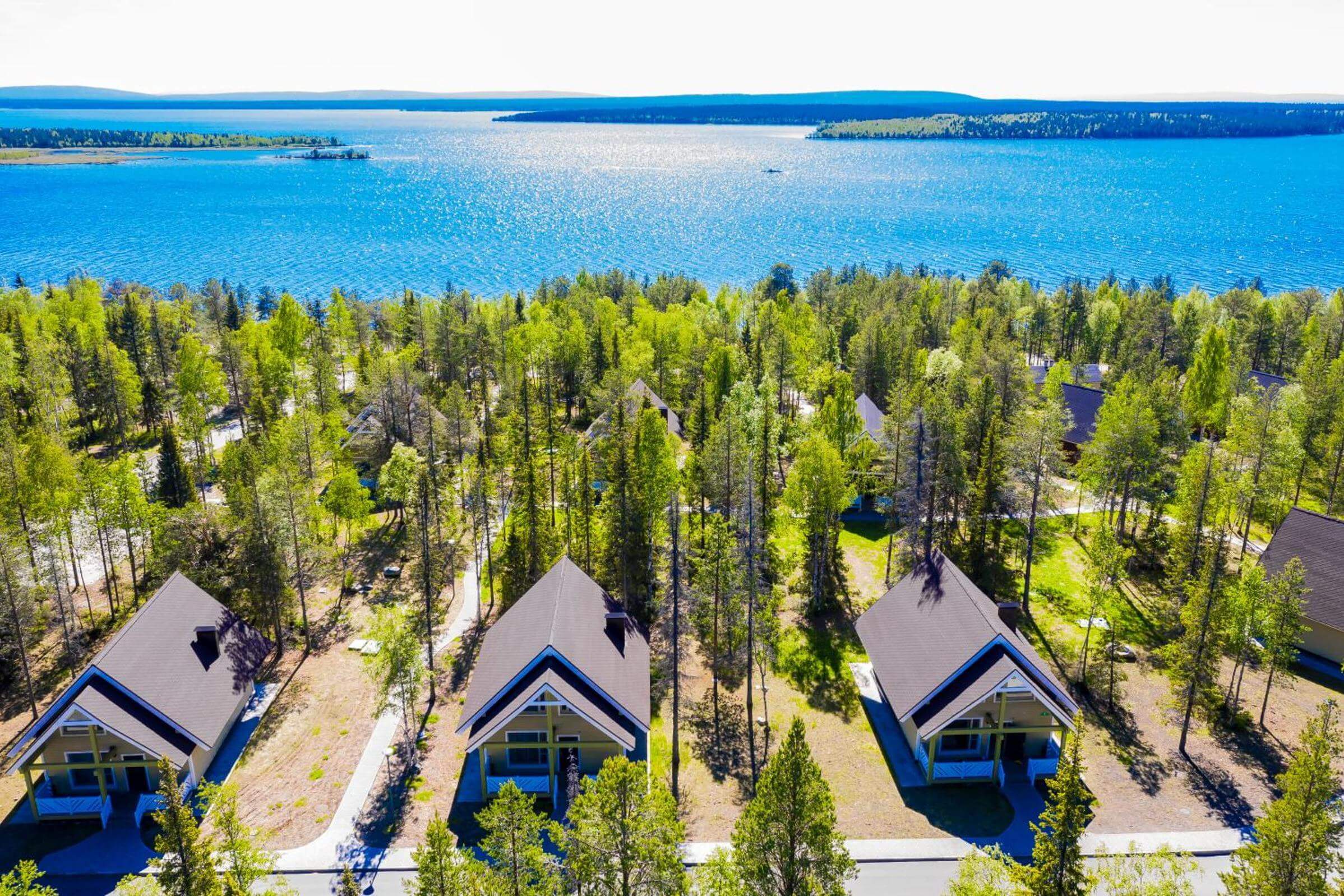 Панорамный вид: домики для отдыха, сосны и озеро.