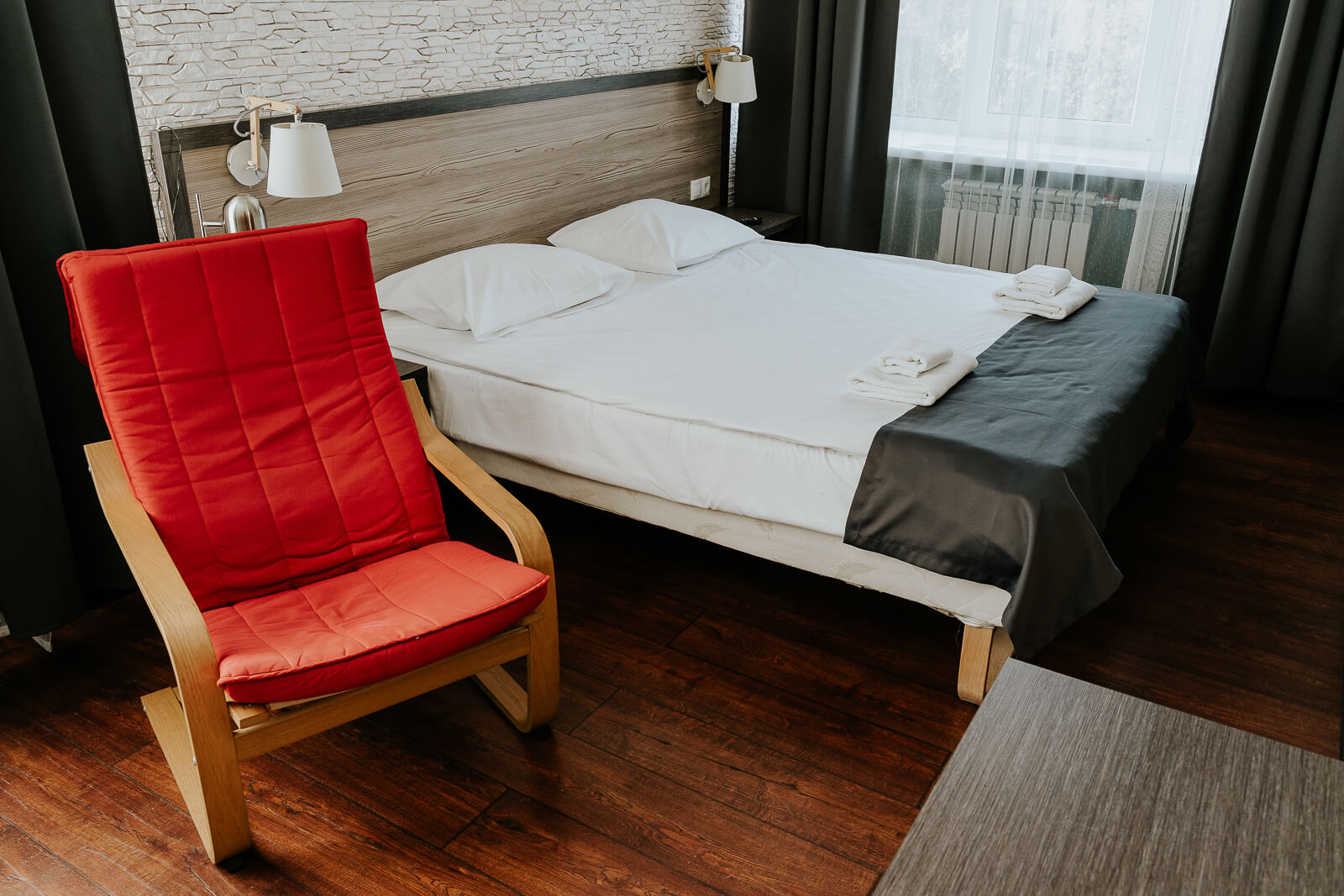 Застеленная кровать и кресло с красными подушками.