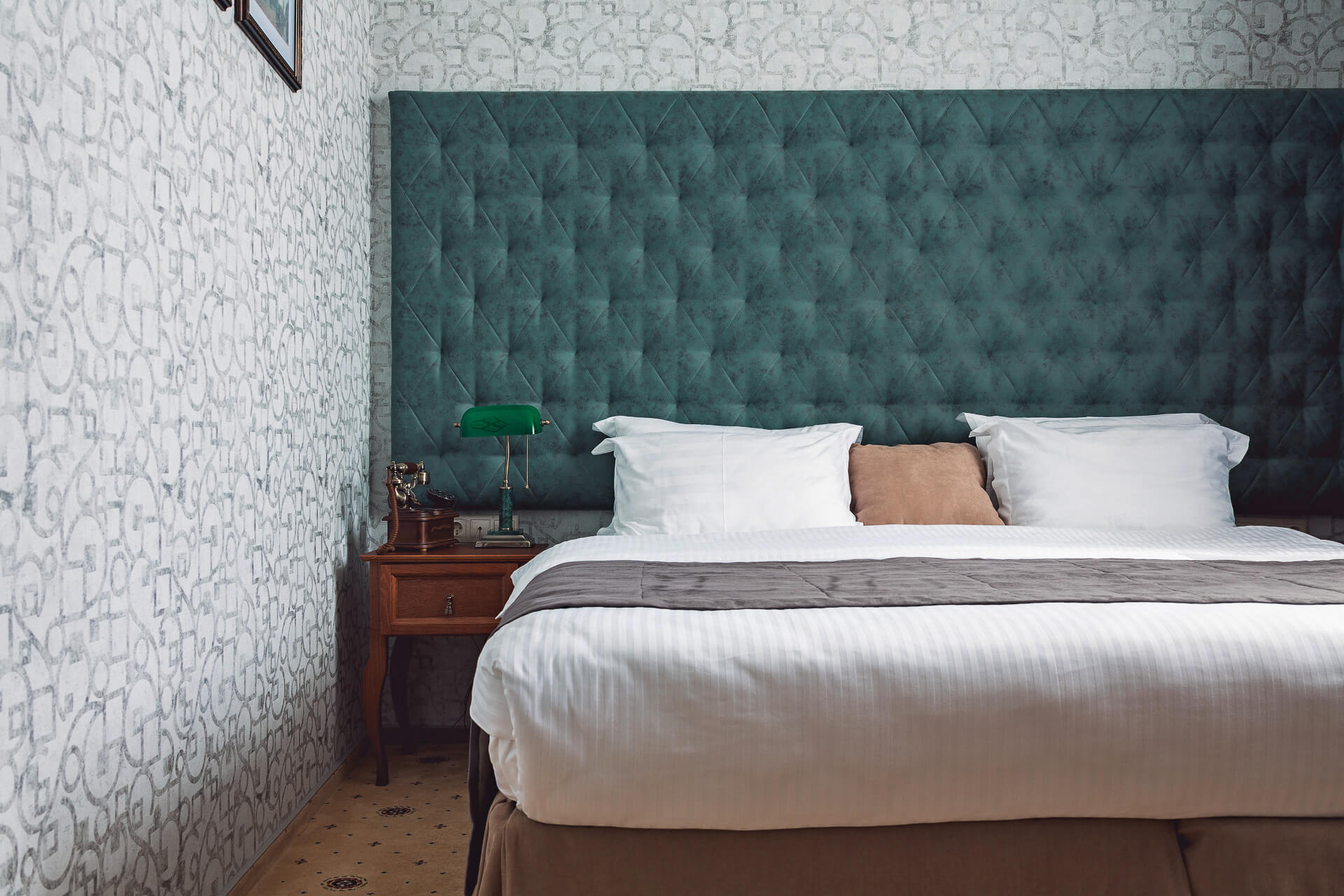 Возле кровать, на прикроватной тумбочке, стоит красивая зеленая лампа.