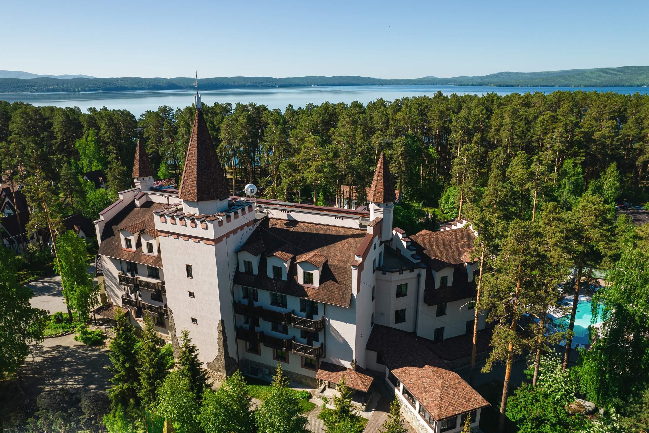 Панорамный вид: здание отеля, похожее на замок и озеро Тургояк.