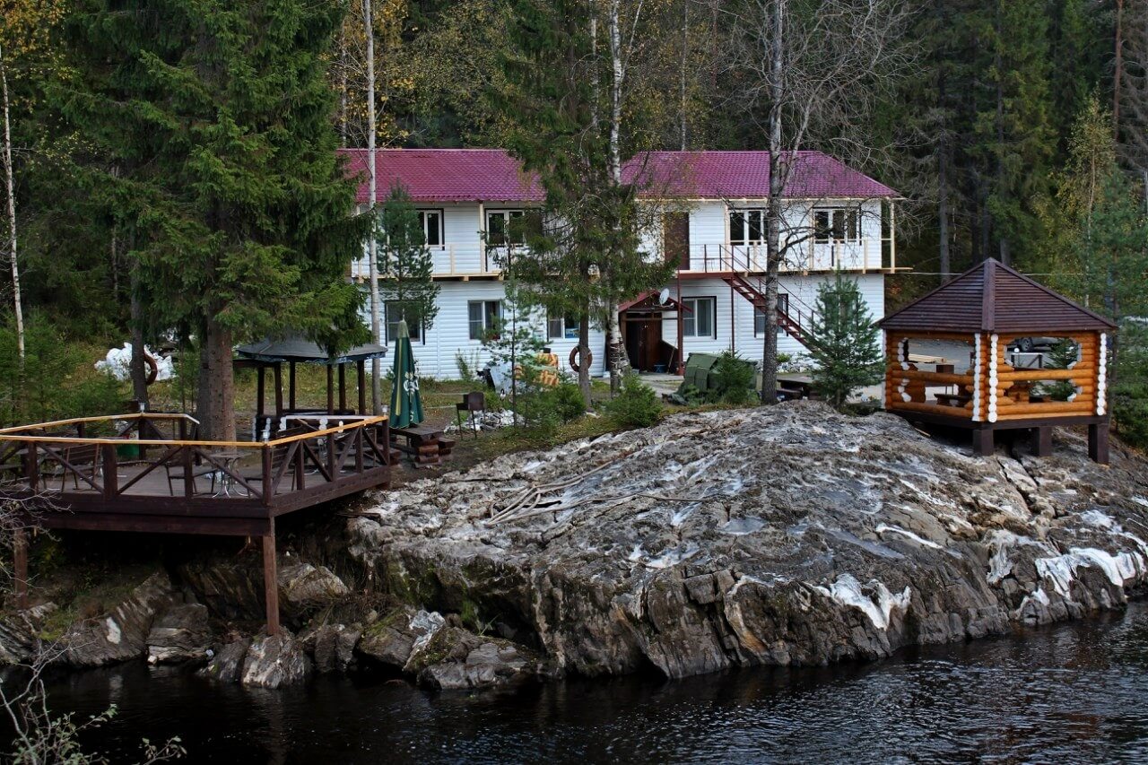 Вид со стороны озера: беседка со смотровой площадкой, гостевой дом и скальные выступы у берега.
