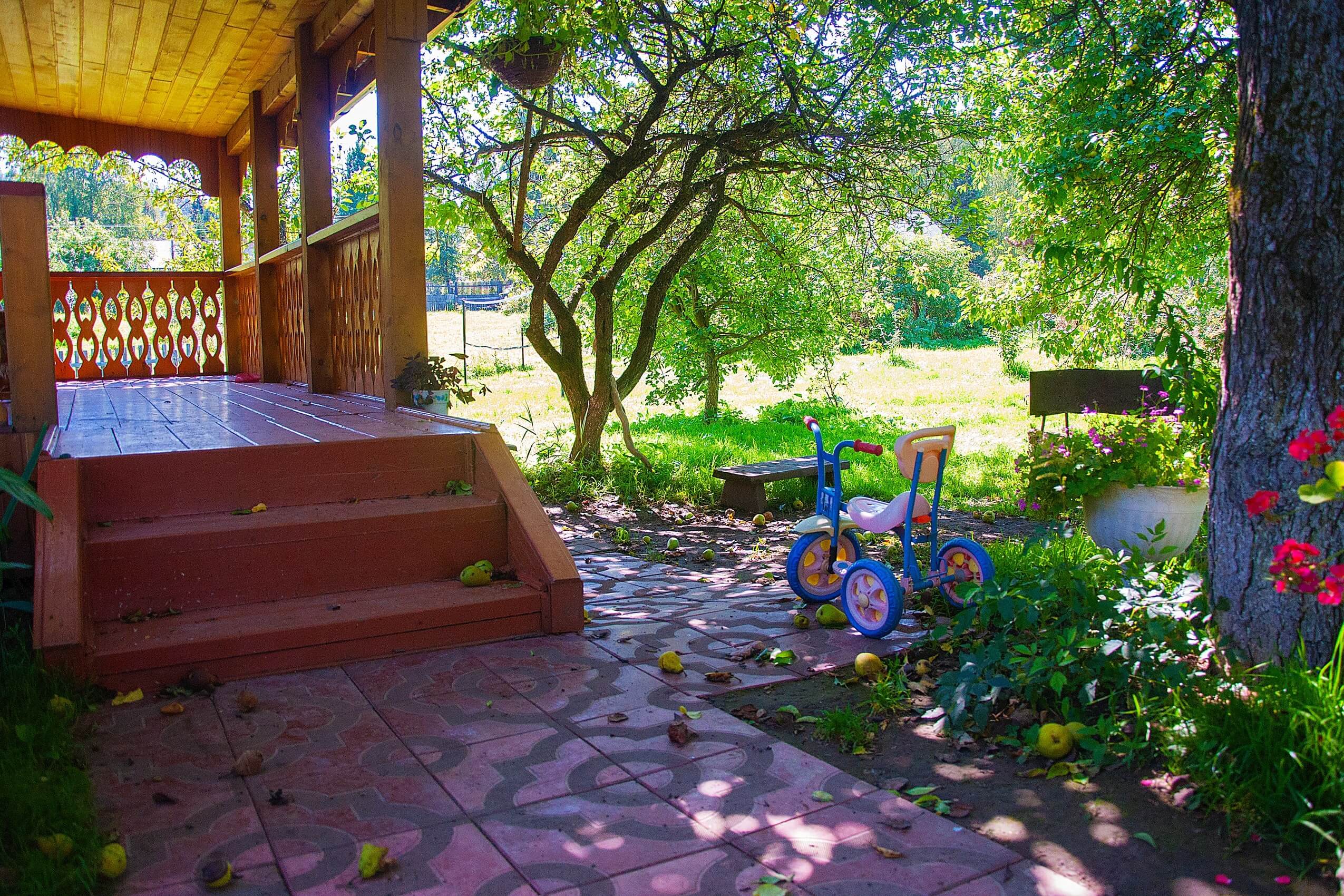 У крыльца на земле лежат яблоки. Стоит детский велосипед.