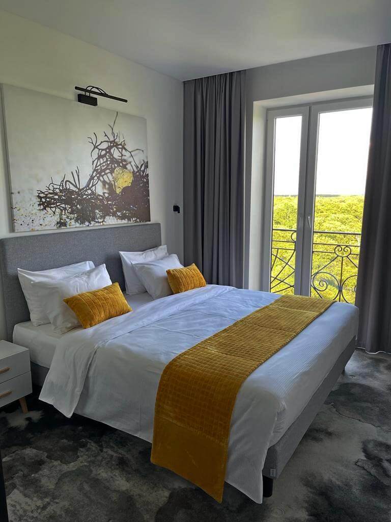 Пример спального места: белоснежное белье, желтые саше и подушки, рядом с кроватью - окно.