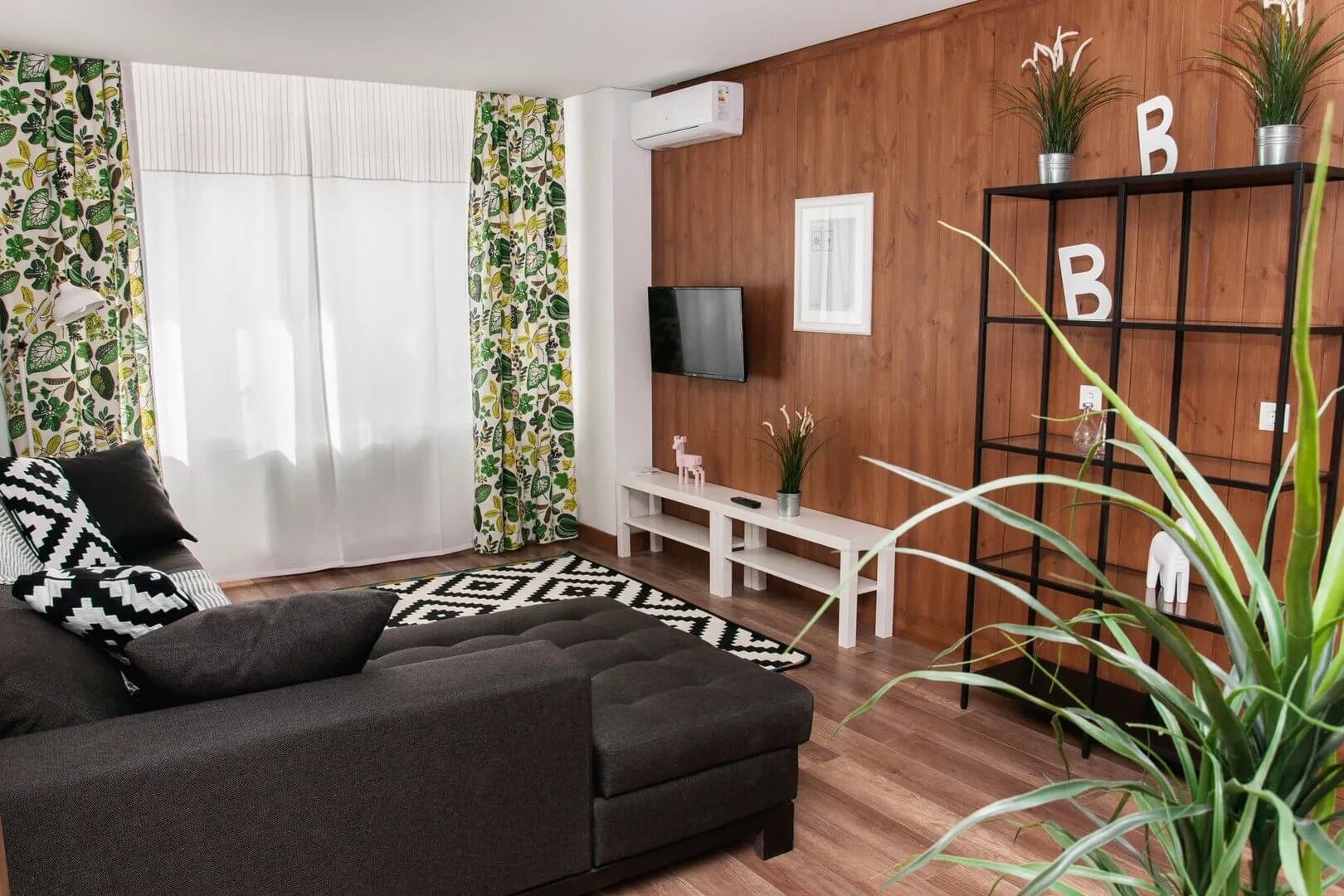 Зона гостиной: большой диван, телевизор на стене, красивые шторы на окнах.