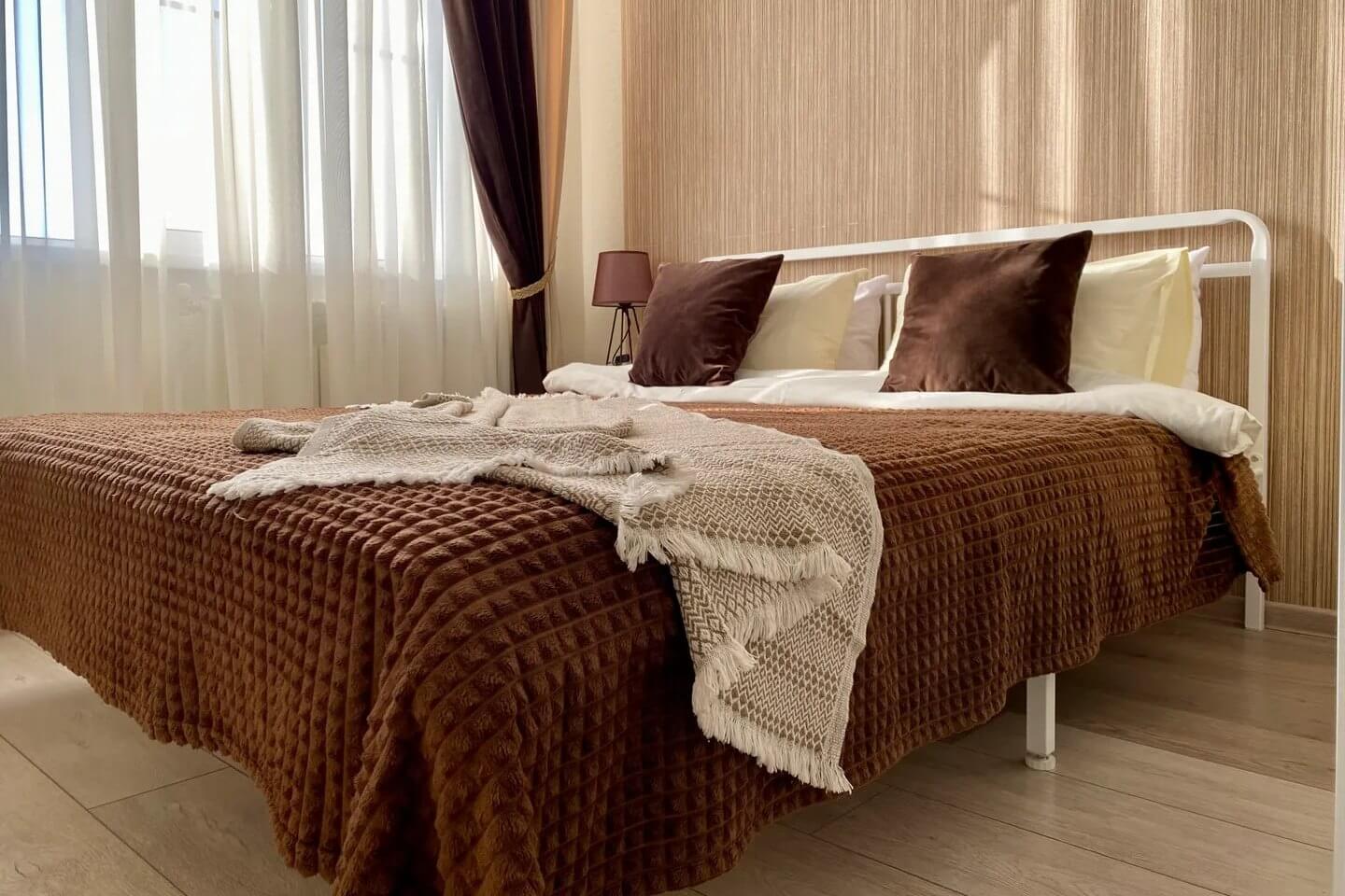 Кровать застелена коричневым покрывалом и накрыта пледом.