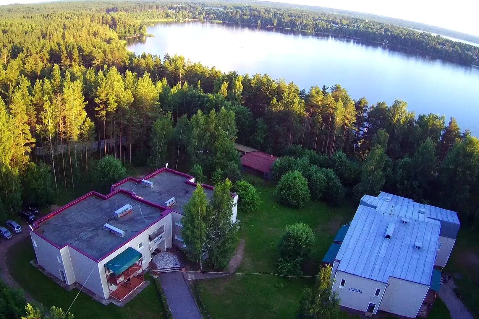 Панорамный вид: два гостевых корпуса, лес и озеро.