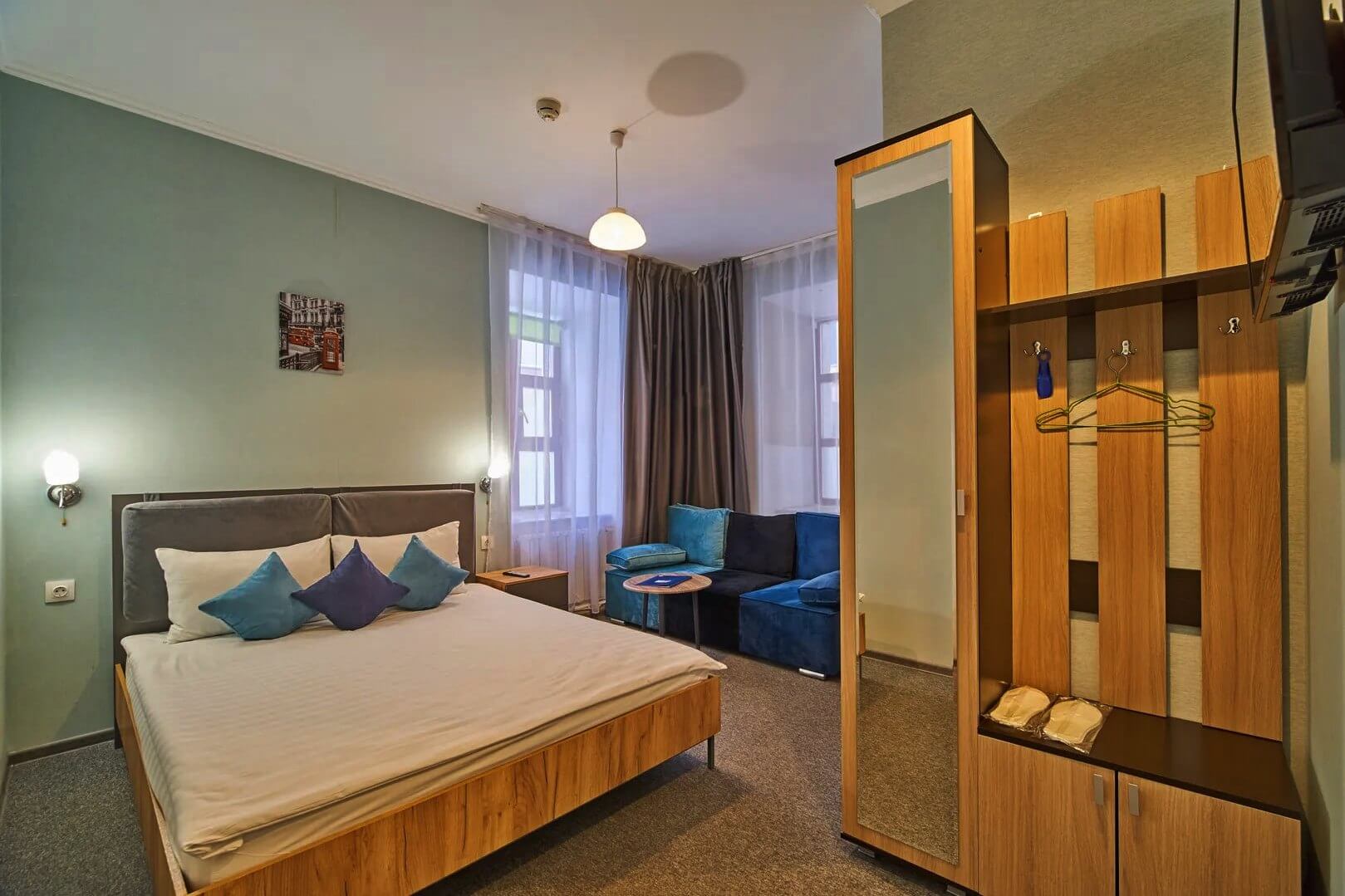 В комнате три отдельных зоны: спальня с кроватью, зона прихожей со шкафом и зеркалом, у окна - диван с кофейным столиком.