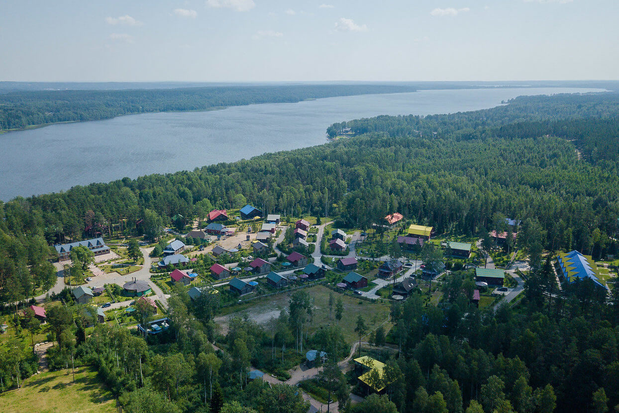 Вид на базу с высоты: крыши домов, лес и озеро.