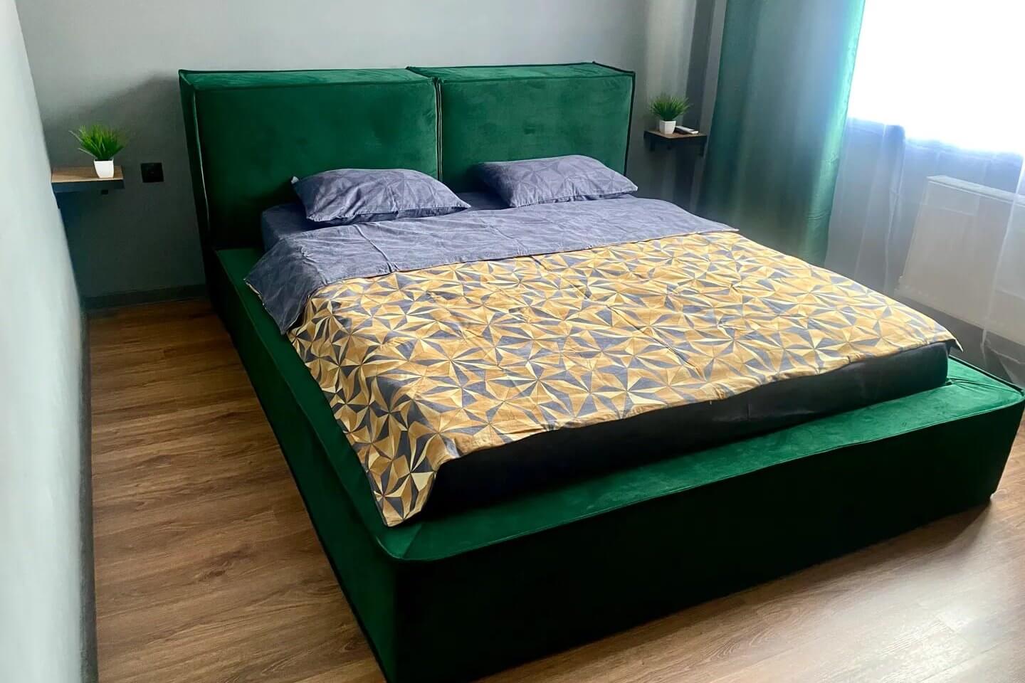 Основание кровати обшито зеленой бархатной тканью.