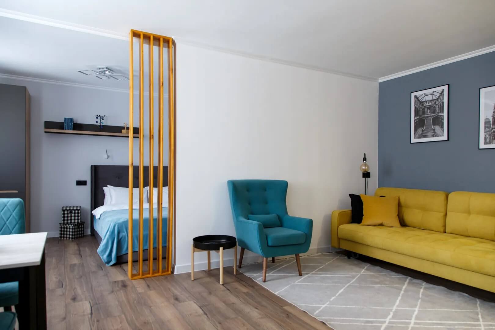 Комната: желтый диван, бирюзовое кресло, за деревянной перегородкой - кровать с бирюзовым покрывалом.