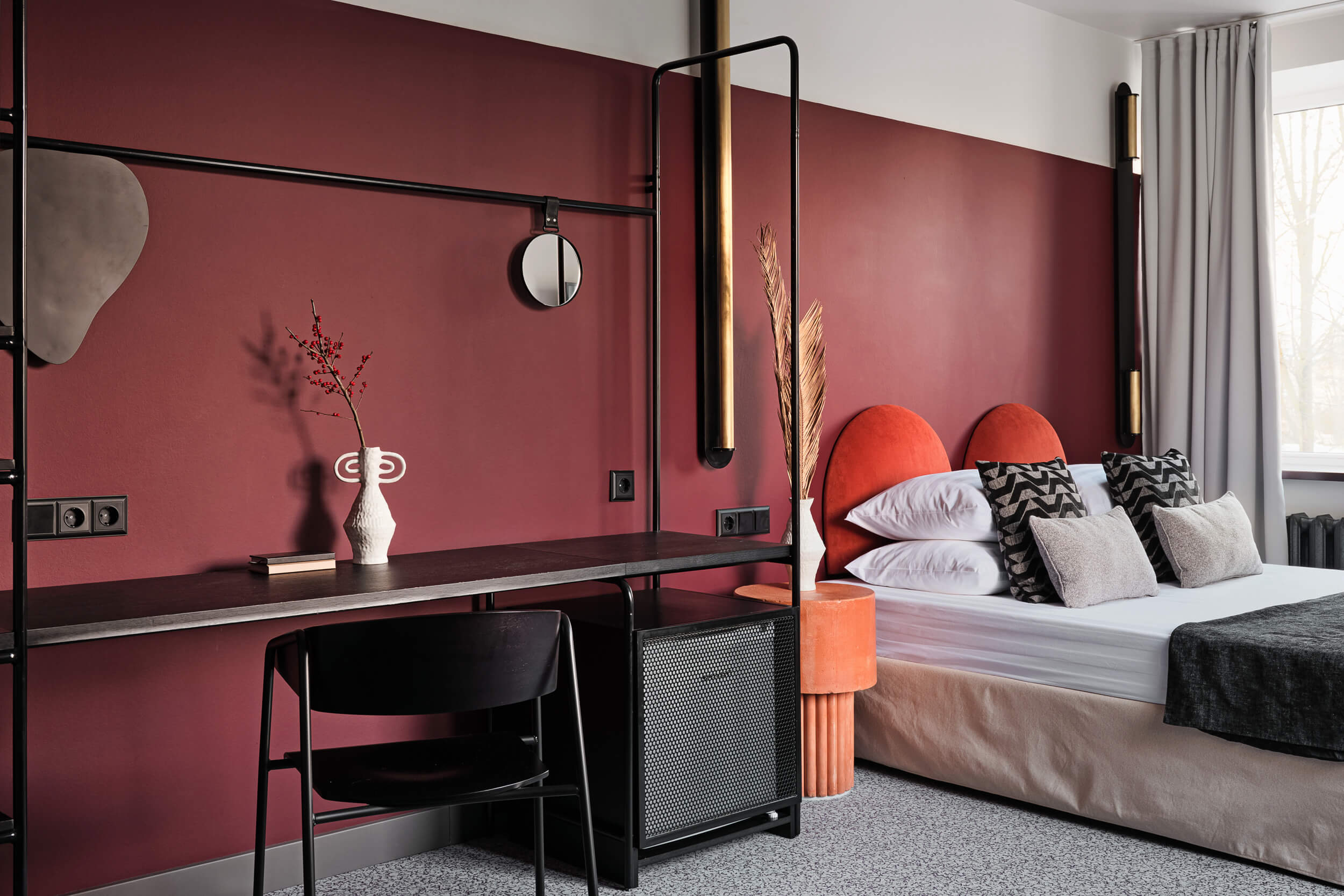 Стена у кровати выкрашена в насыщенный бордовый цвет.