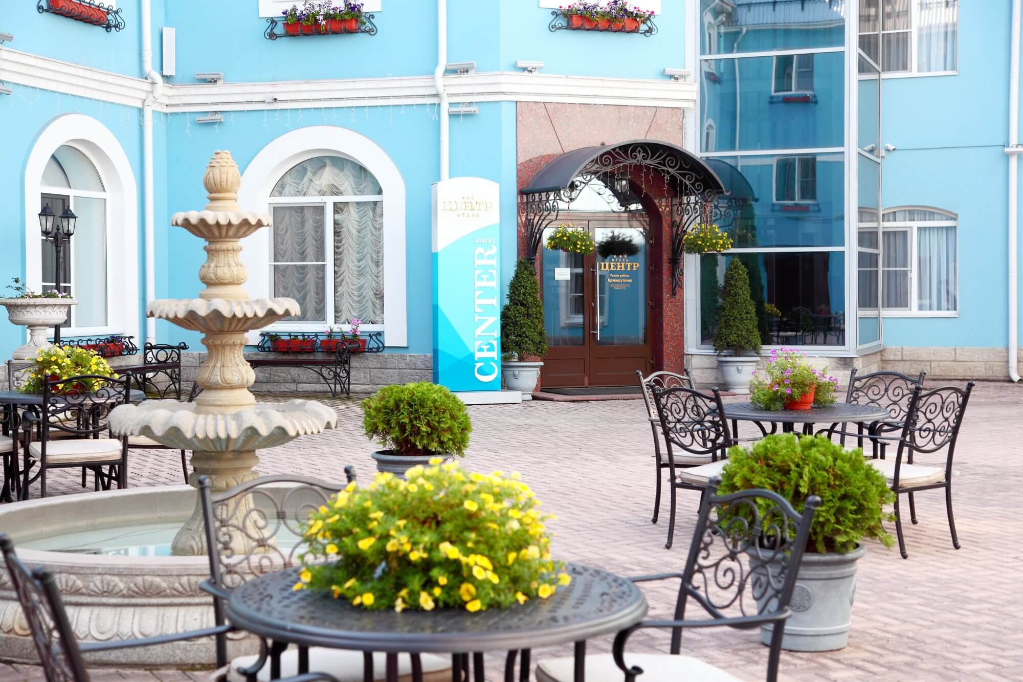 Внутренний двор: столики кафе и фонтан. Фасад здания - голубого цвета.