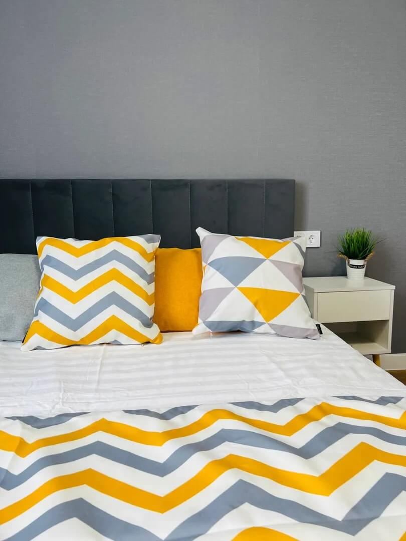 Кровать застелена ярким постельным бельем в желто-серую полоску.