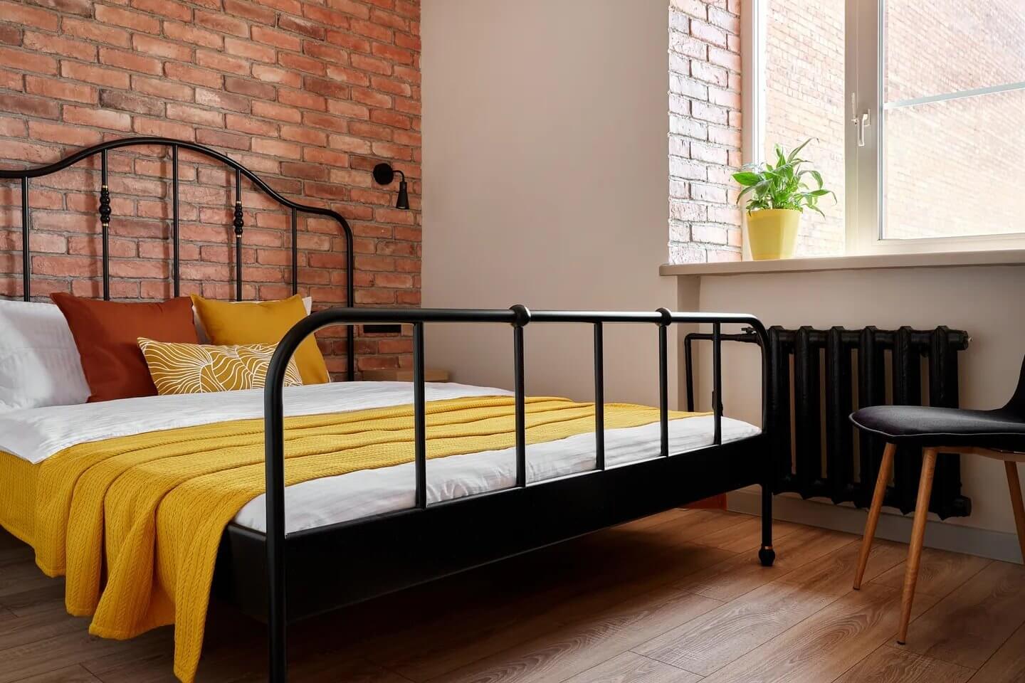 Кровать с желтым покрывалом и красно-кирпичная кладка.