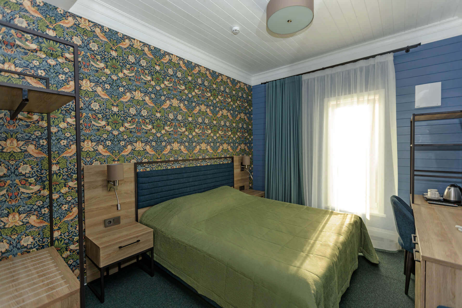 Цвет интерьера: зеленый, синий и белый. На стене у кровати - красивые обои с узором.