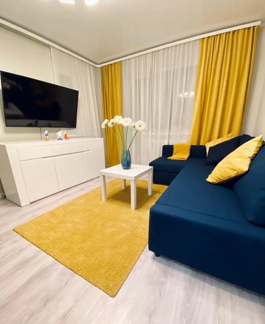 Шторы, коврик на полу и подушки на диване - желтого цвета.