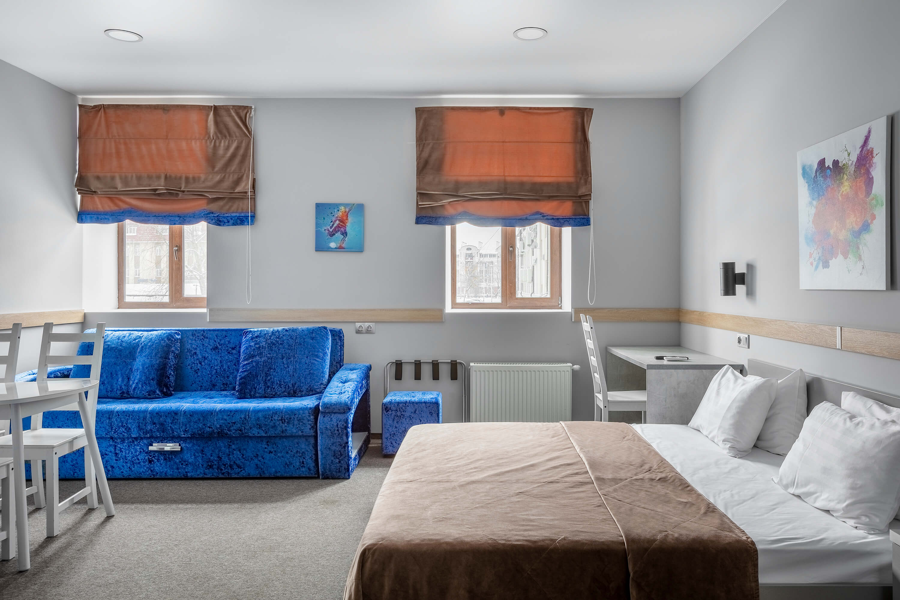 Комната: кровать, синий диван, два окна.