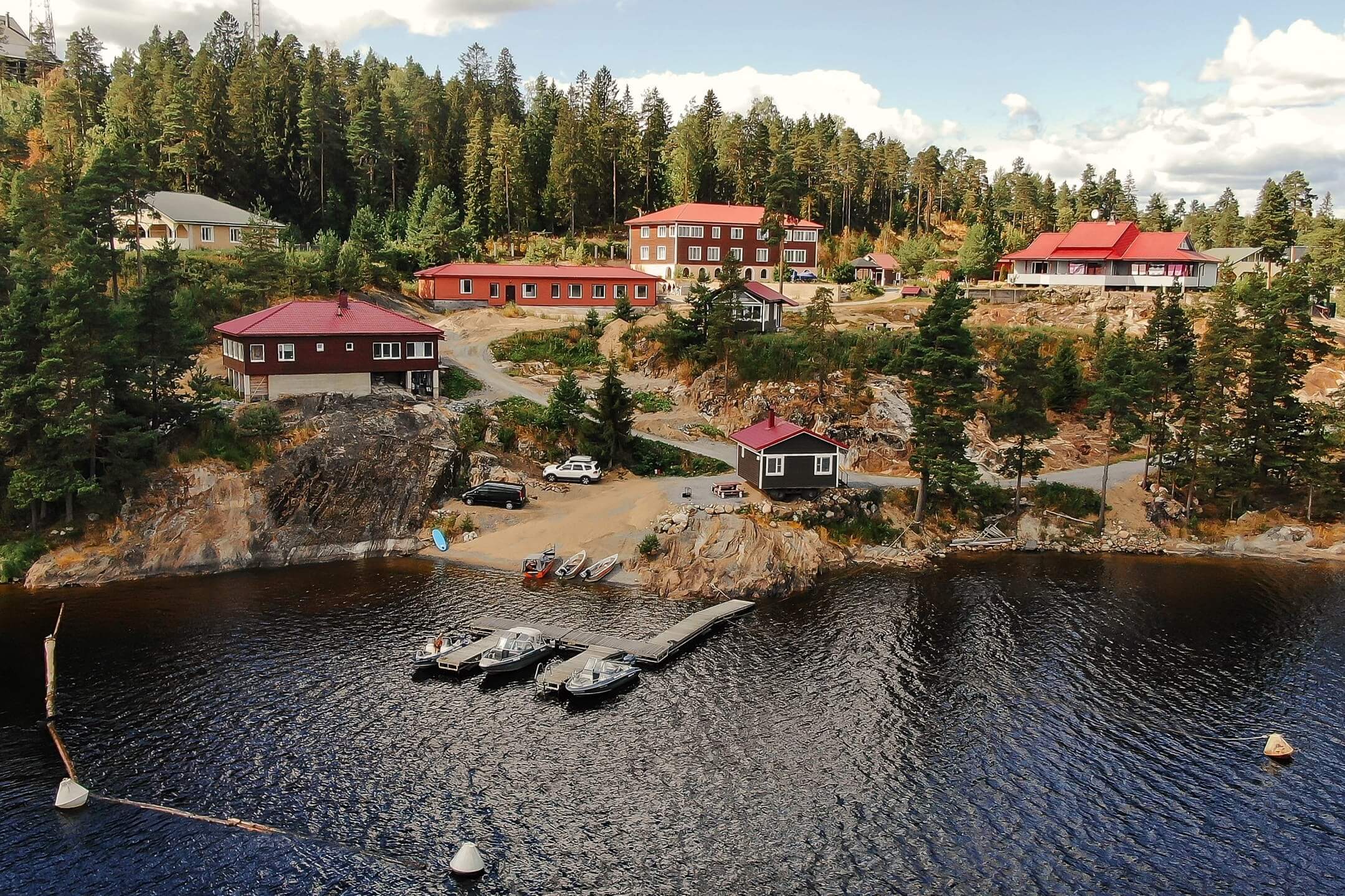 Панорамный вид на территорию базы отдыха: скалы, лес и озеро, красные крыши домов.