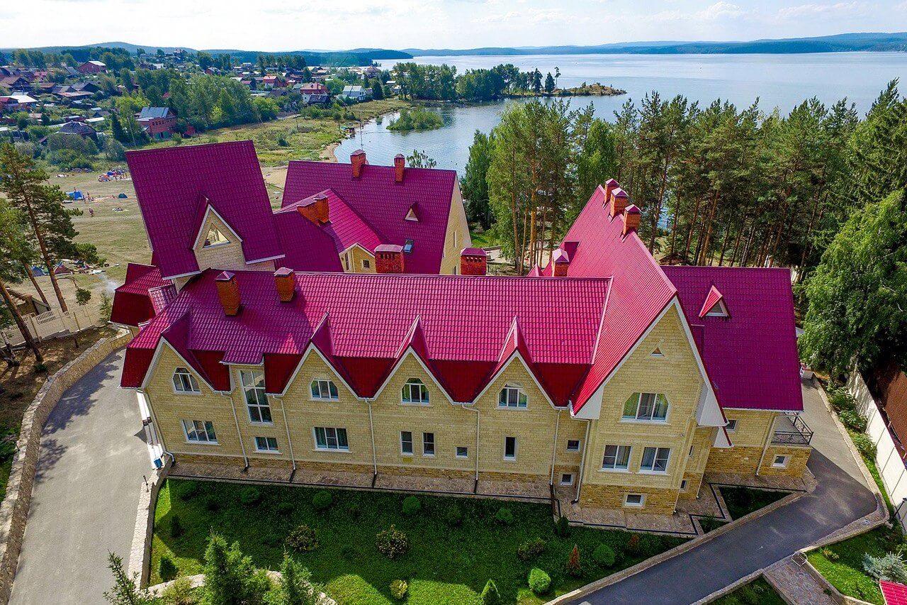 Панорамный вид: бордово-малиновая крыша отеля и озеро вдали.