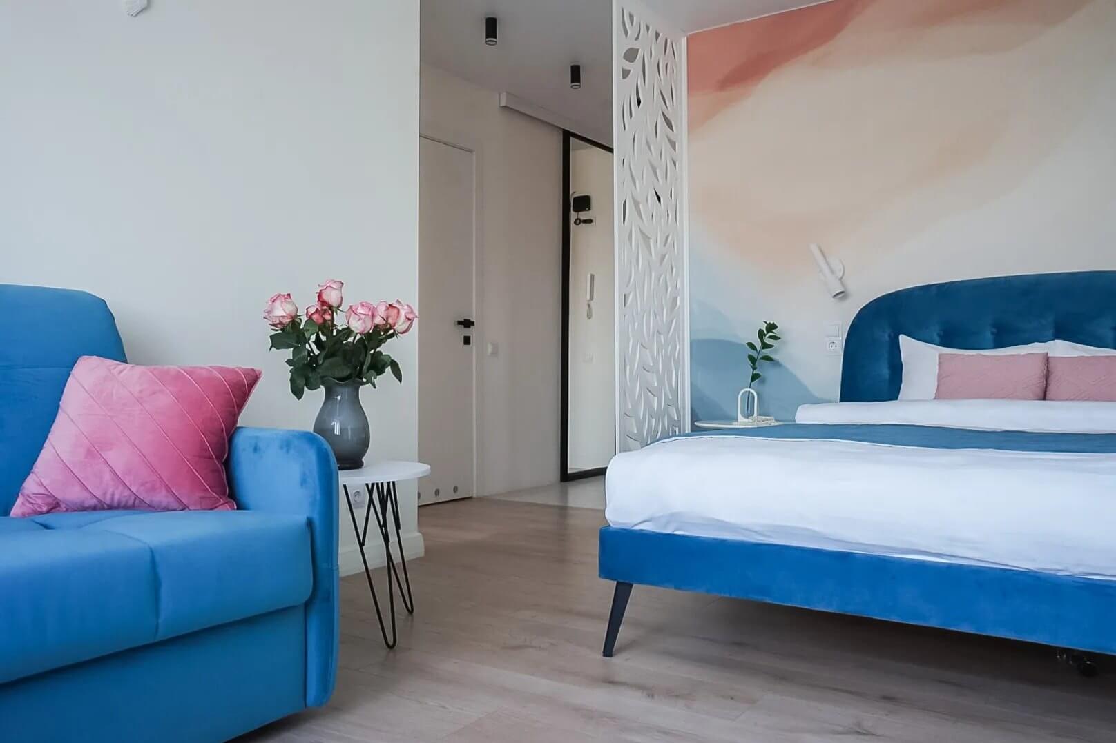 У кровати и дивана - красивая синяя обивка. Подушки - розовые.