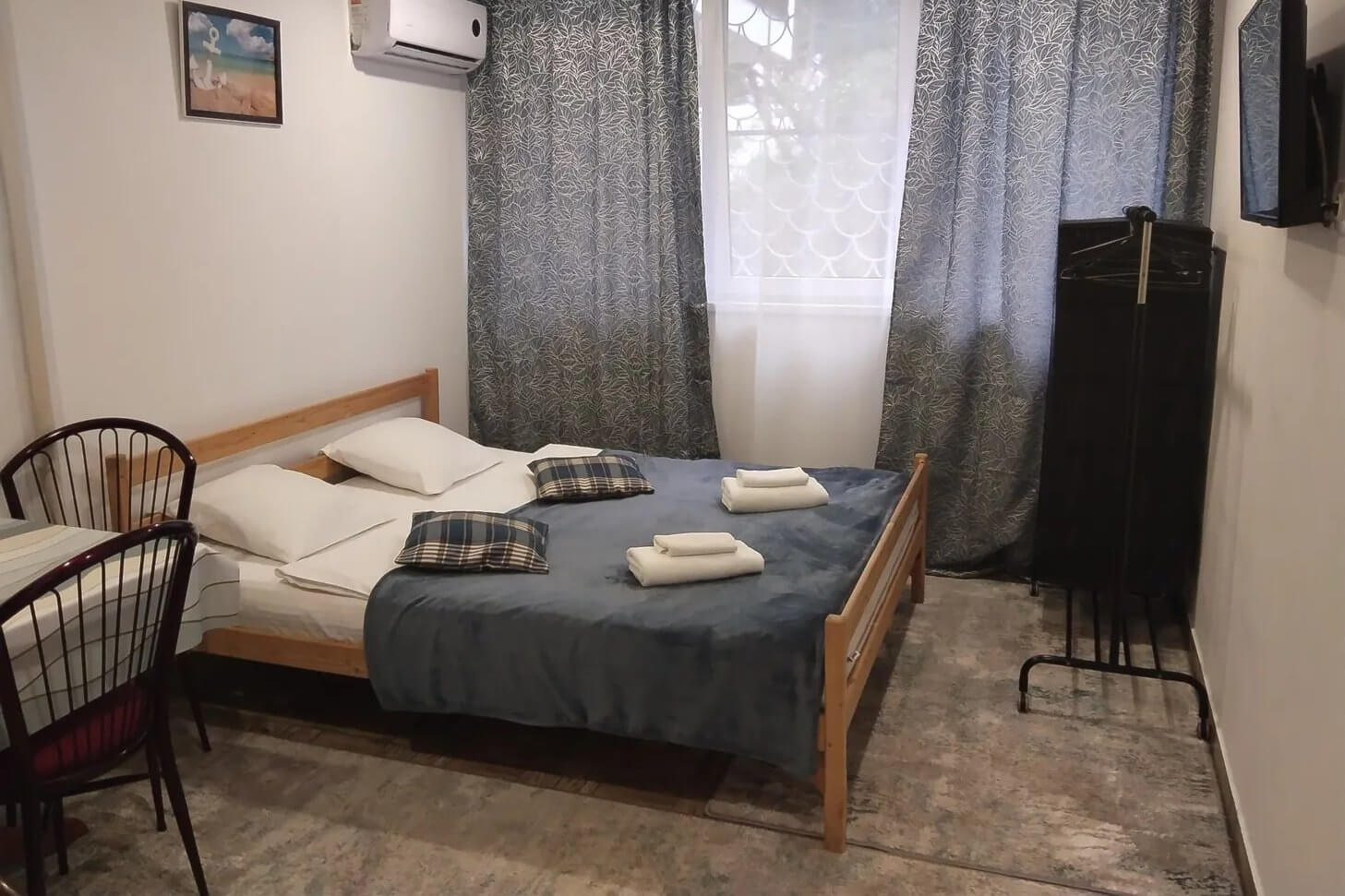 Спальня: кровать с деревянным основанием, вешалка для вещей, зашторенное окно.
