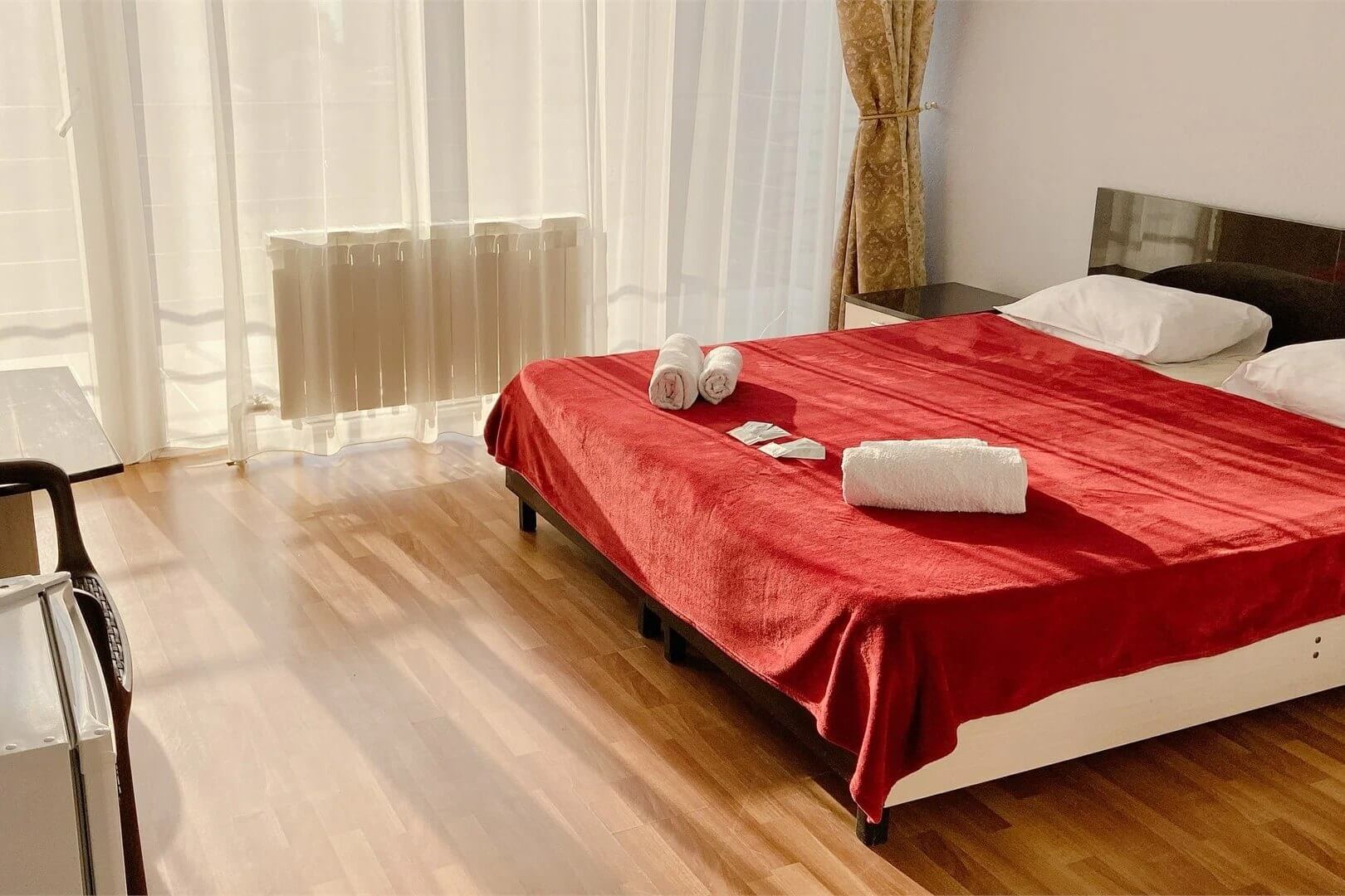 Кровать в номере накрыта красным покрывалом.